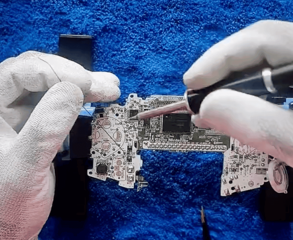 RetroGear-moddingtekniker, der lodder et Nintendo Game Boy Advance-motherboard, mens han har hvide handsker på.